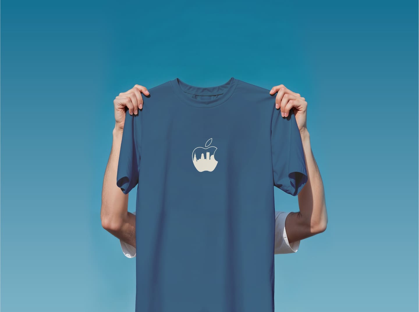 Two hands holding up a blue t-shirt against a clear sky. A cream Apple logo on the chest is filled with the Buffalo skyline.